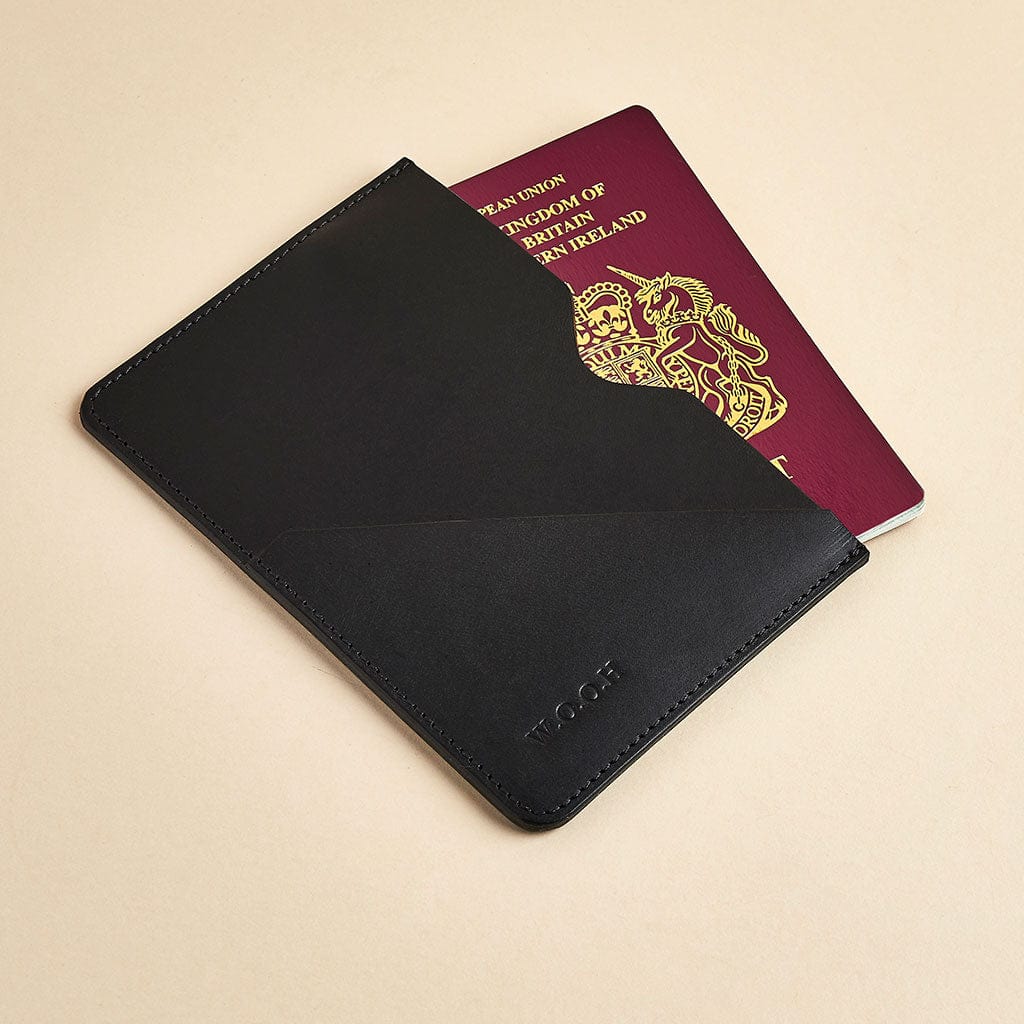 Black leather passport sleeve with personalised initials, shown with a British passport - made by Man & Bear