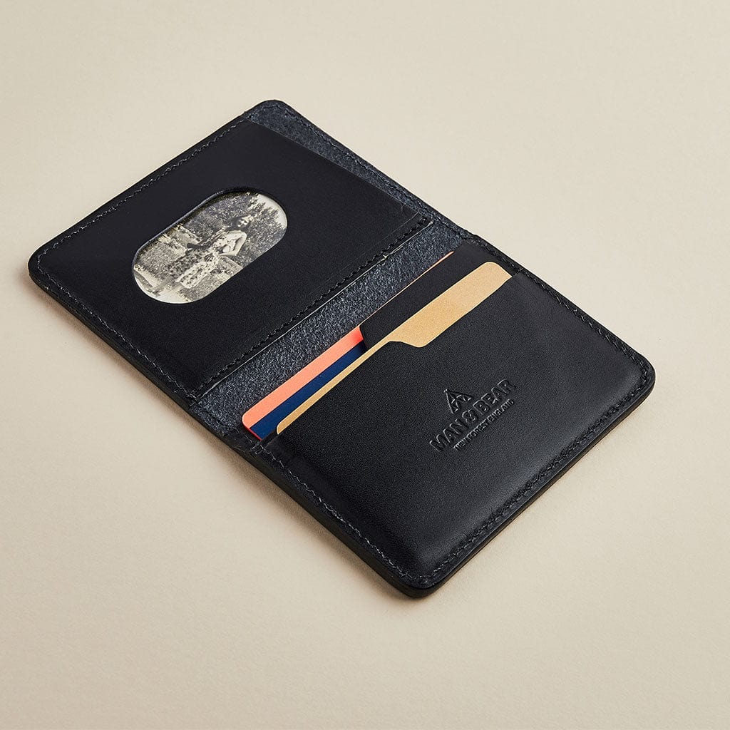 A black leather men's wallet with card slots, showing the Man & Bear logo