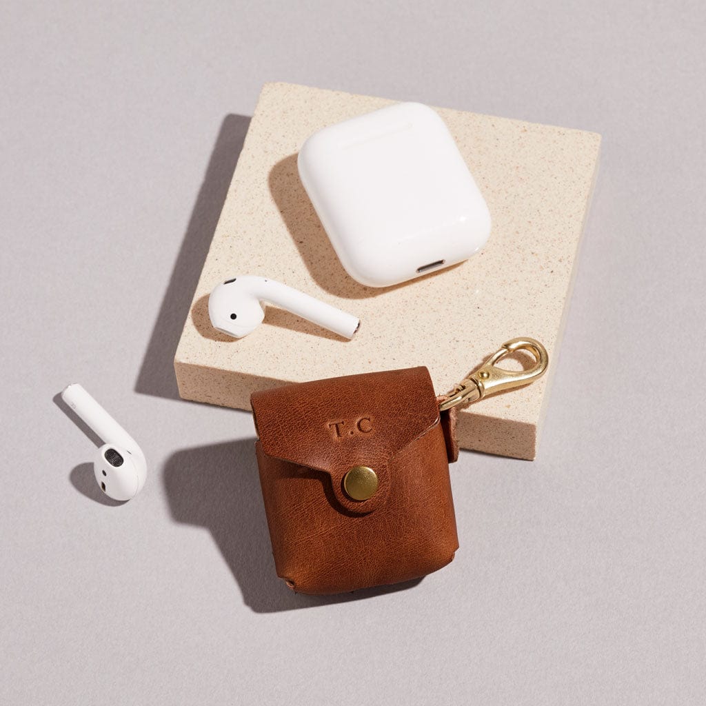 Brown leather AirPod case with personalised initials, shown with headphones