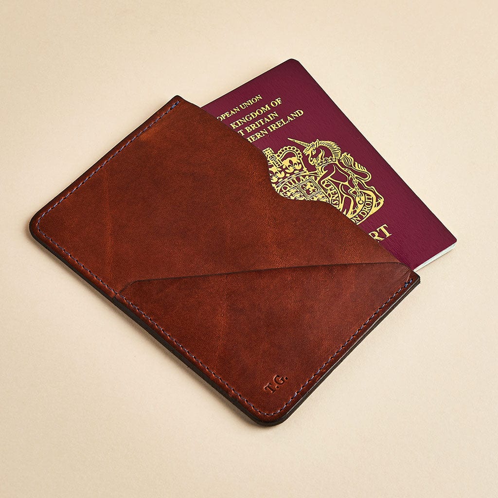 Brown leather passport sleeve with personalised initials, shown with a British passport - made by Man & Bear