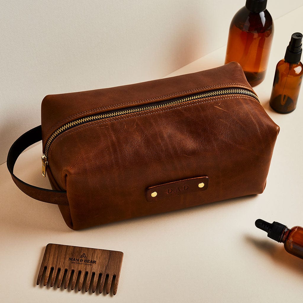 Brown leather men's wash bag with personalised initials, made by Man & Bear, shown with comb and toiletry bottles